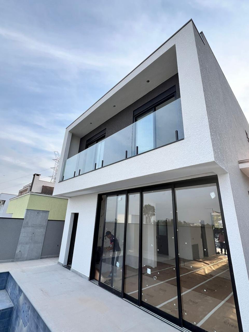 Fachada residencial com guarda-corpo de vidro, janelas integradas e portas de correr com perfis pretos